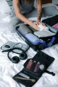 One Bag, Any Adventure: Carry-On Only Packing Lists for City Breaks & Outdoor Escapes 9 Person organizing suitcase with clothes and toiletries on bed, preparing for travel.